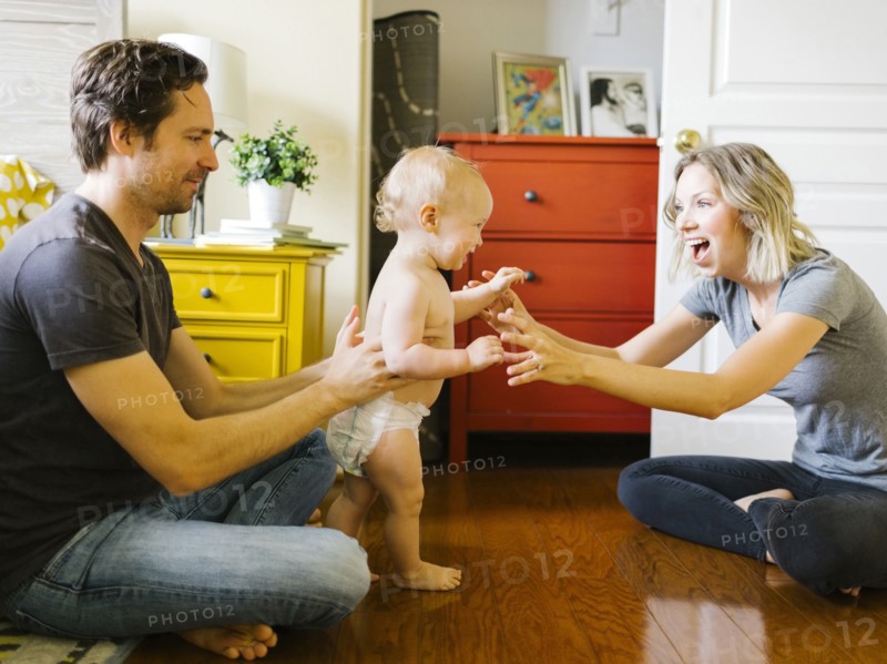 Baby boy (12-17 months) taking first steps with parents at home
