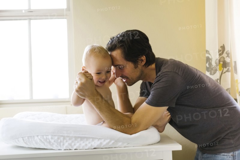 Father playing with baby boy (12-17 months) on changing mat