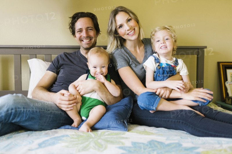 Portrait of parents sitting with sons (12-17 months, 4-5) on bed