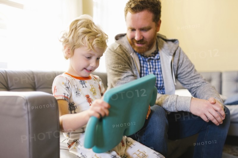 Boy (4-5) and man using digital tablet on sofa in living room