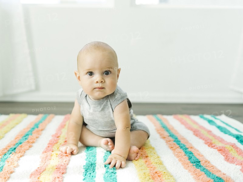 Portrait of baby boy (6-11 months) sitting on colorful carpet