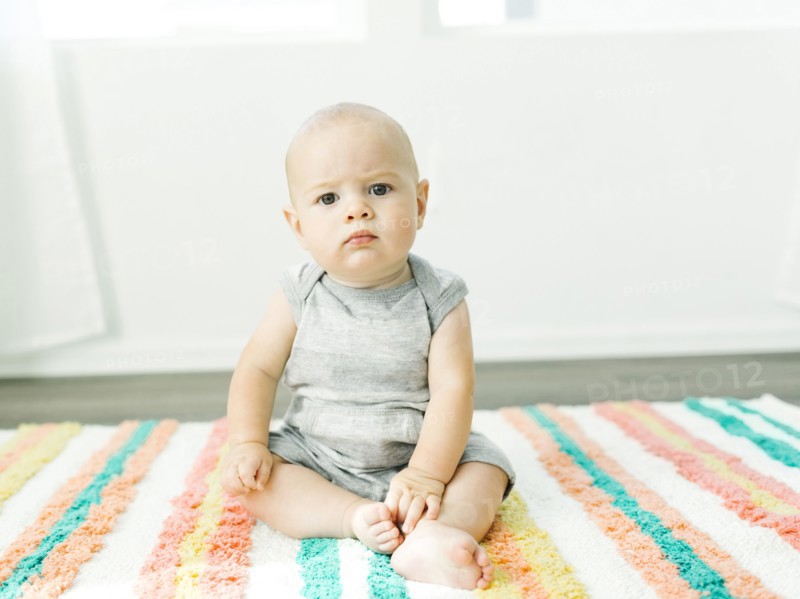 Portrait of baby boy (6-11 months) sitting on colorful carpet