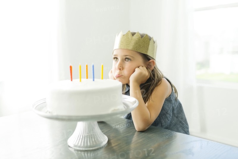 Sad girl (6-7) with birthday cake