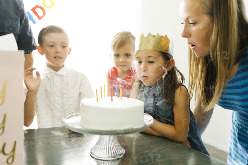 Brothers (2-3, 6-7) looking at sister (6-7) and mother blowing birthday candles