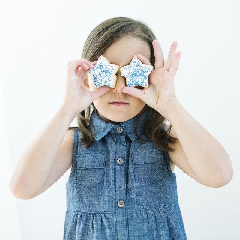 Girl (6-7) holding cookies in front of eyes