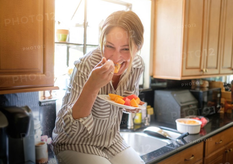 Woman in kitchen eating fruit salad