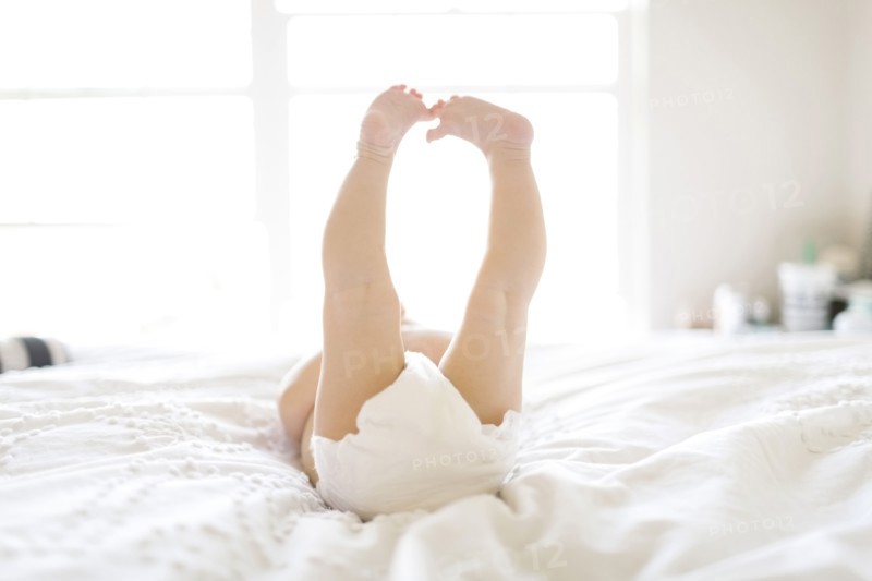 Baby girl (6-11 Months) lying down on bed with feet in air