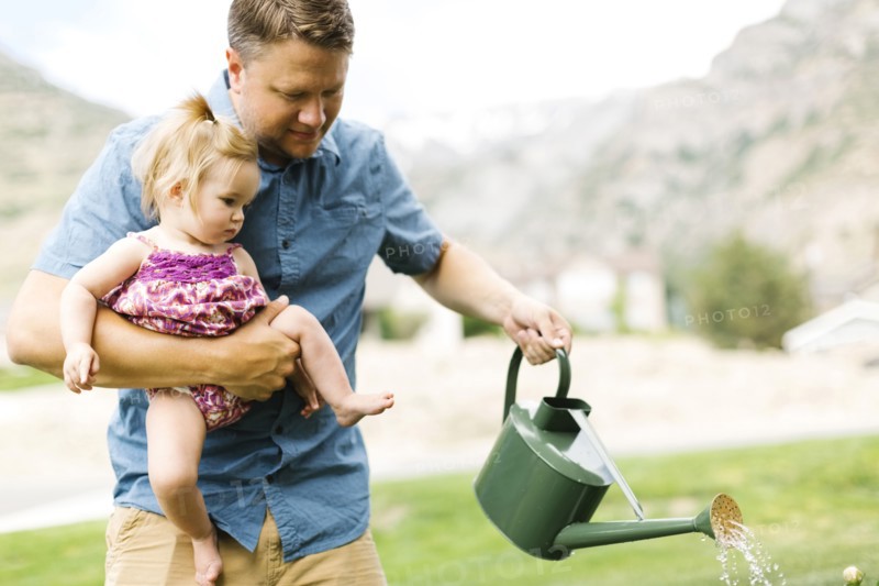 Father with baby girl (12-17 months) watering plants in backyard