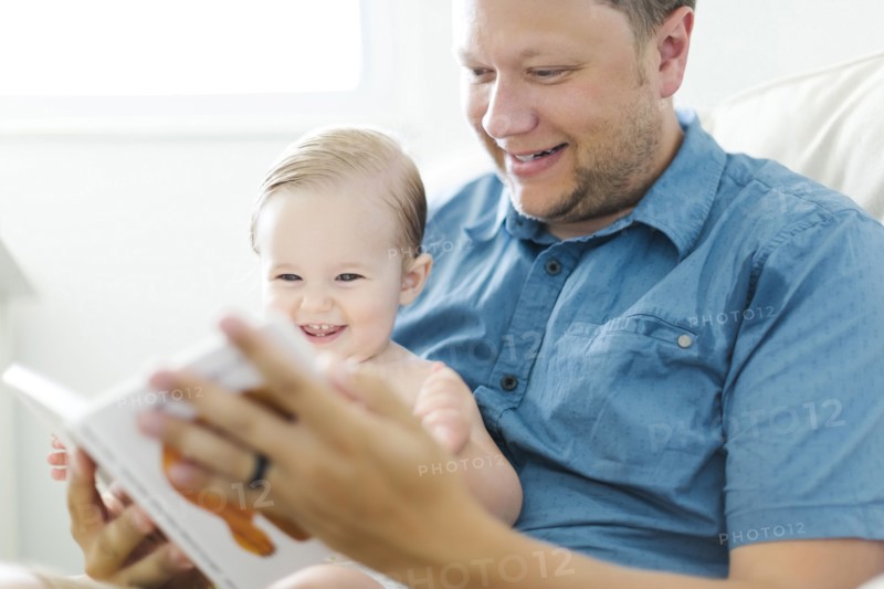 Father with baby girl (12-17 months) sitting in living room and reading book