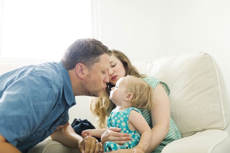 Mother and father with baby girl (12-17 months) sitting in living room and kissing