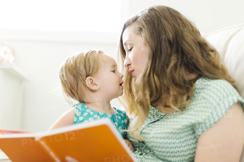 Mother with baby girl (12-17 months) sitting in living room and reading book