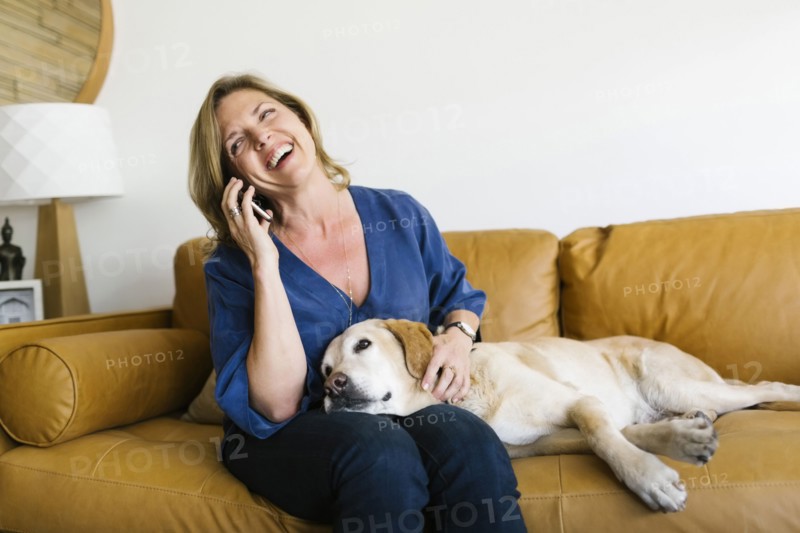 Woman stroking Labrador Retriever and using mobile phone