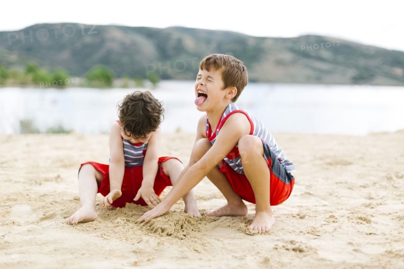 Brothers (4-5, 6-7) playing on beach by lake