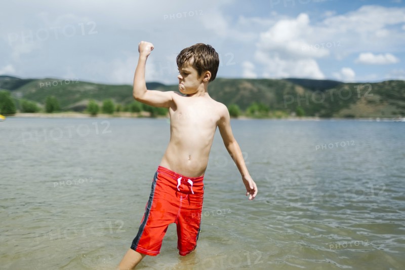 USA, Utah, Park City, Boy (6-7) flexing muscles while wading in lake