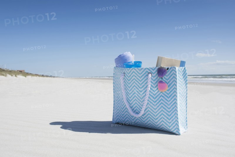 Bag with towel, book and sunglasses on empty beach