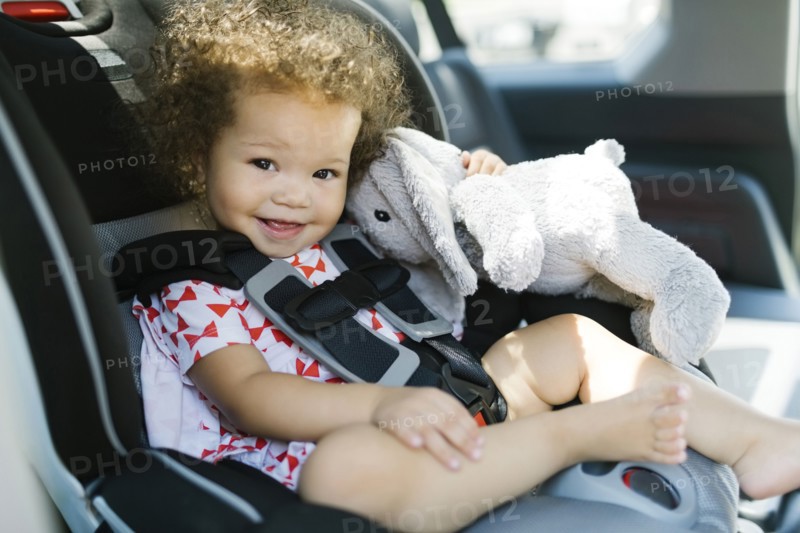 Girl (12-17) sitting on car seat and holding plush toy