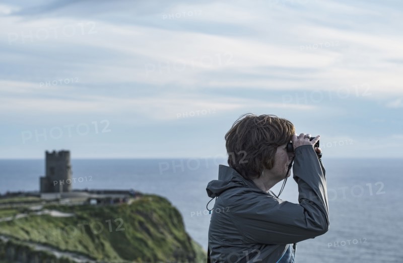 Ireland, Clare County, Woman looking through binoculars on Cliffs of Moher
