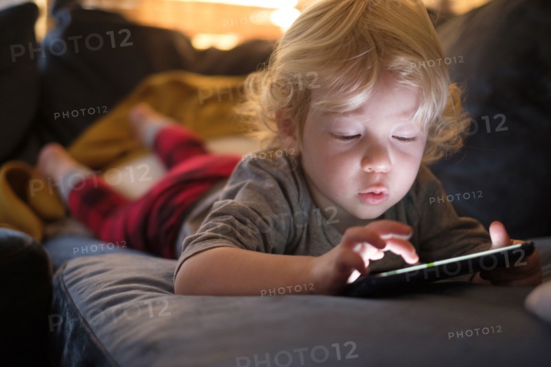 Little boy (2-3) lying on front and playing game on smart phone