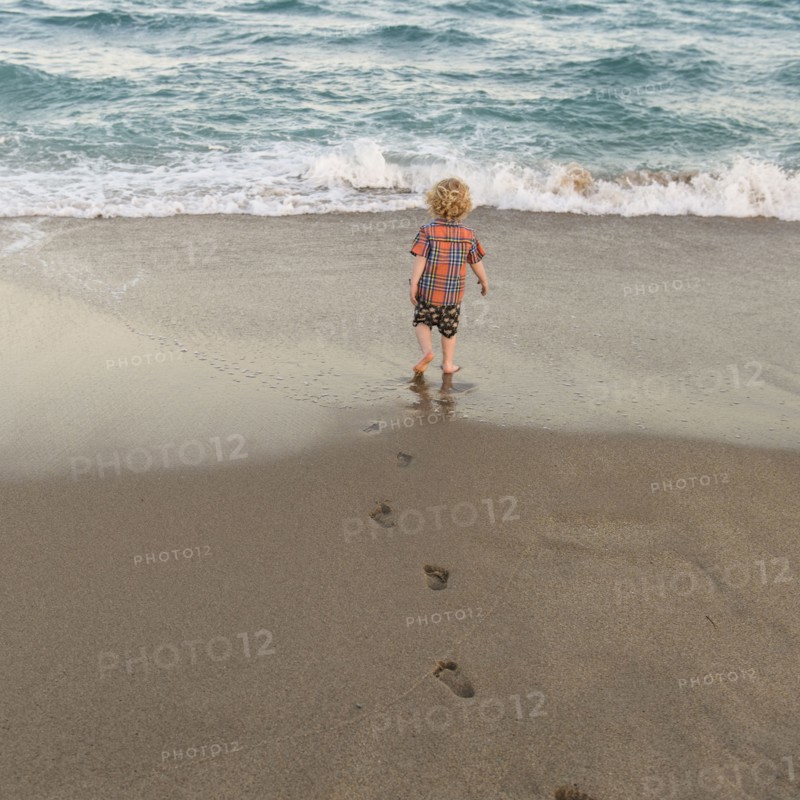 Rear view of little boy (2-3) walking on sandy beach