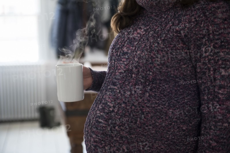 Pregnant woman holding mug with hot beverage