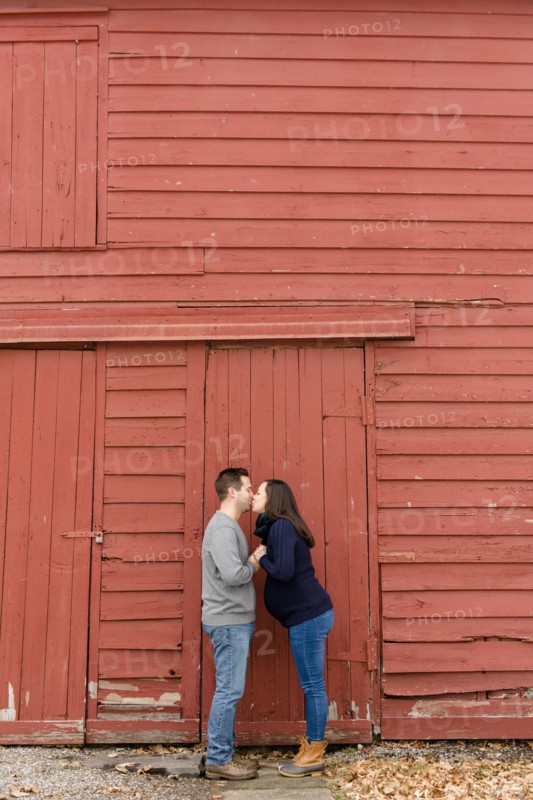 Couple kissing in front of red barn