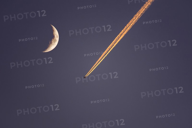Plane flying next to moon at dusk