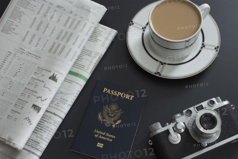 Passport, coffee, old camera and newspapers lying on table