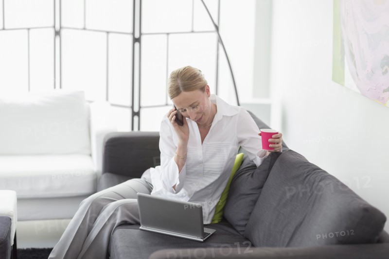 Woman talking on phone and using laptop in living room