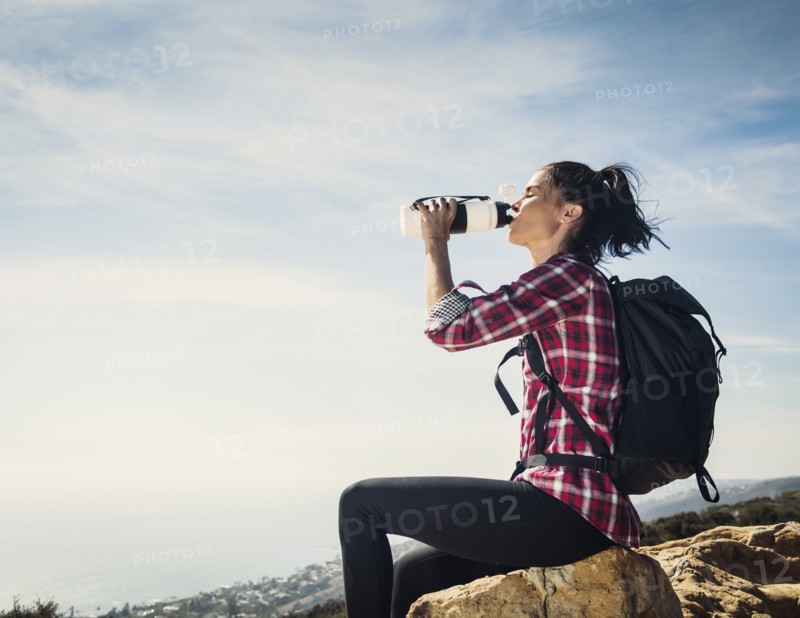 Woman on hike drinking water while sitting on rock