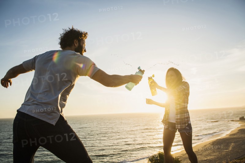 Couple having water fight on beach at sunset