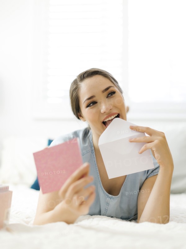 Woman licking envelope on bed