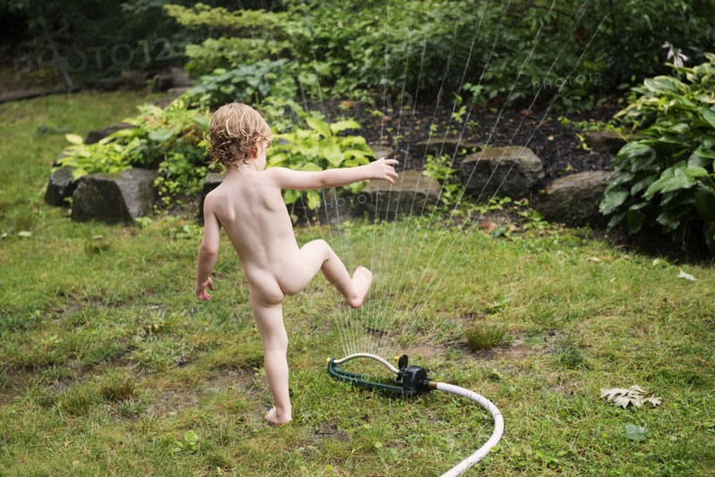 Naked boy playing with sprinkler