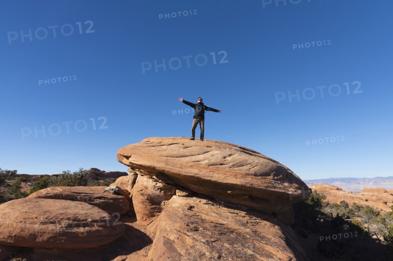 Man with arms outstretched on rock in Arches National Park, Utah, USA