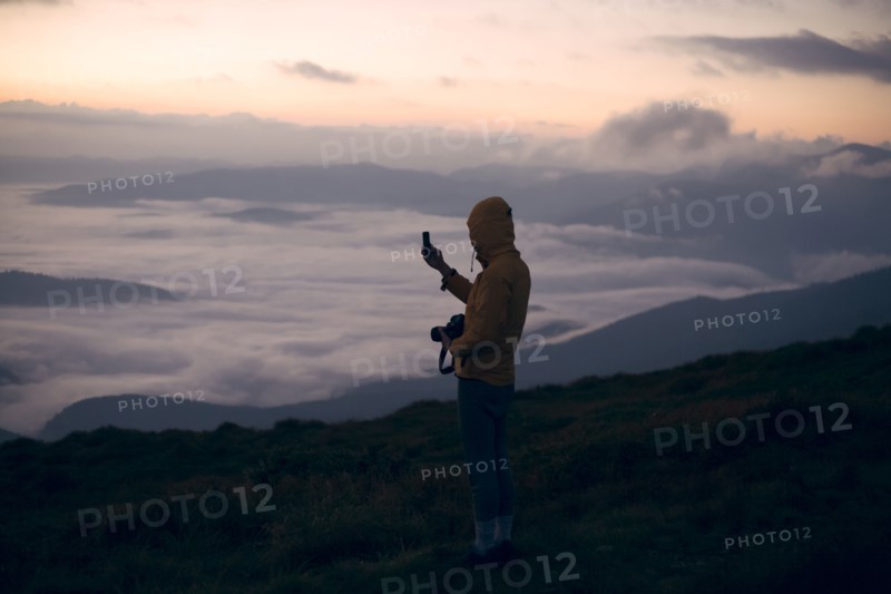 Young man photographing with smart phone at sunset in the Carpathian Mountain Range