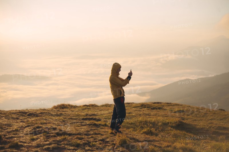 Man in yellow jacket taking photograph on smart phone in the Carpathian Mountain Range