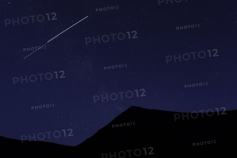 Shooting star above silhouette of mountain