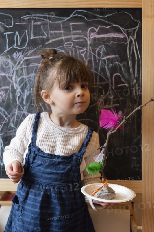 Girl holding stick and feather craft by blackboard