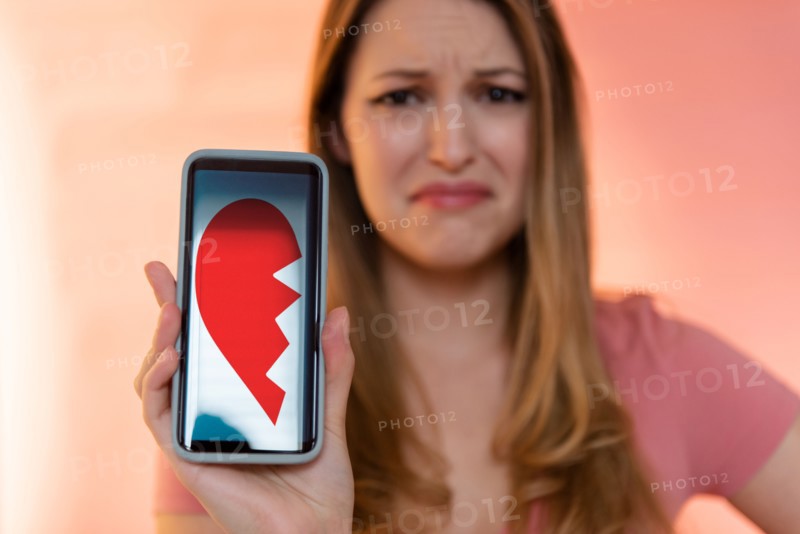 Young woman holding smart phone displaying broken heart