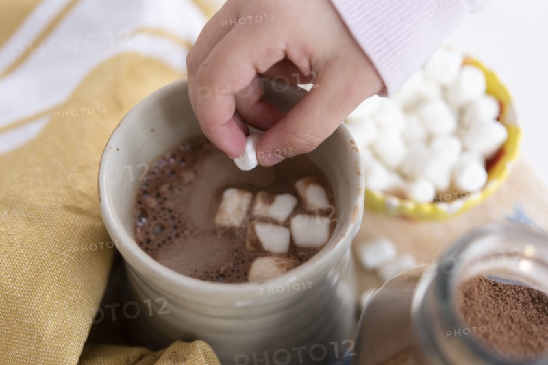 Girl's hand putting marshmallows in hot chocolate