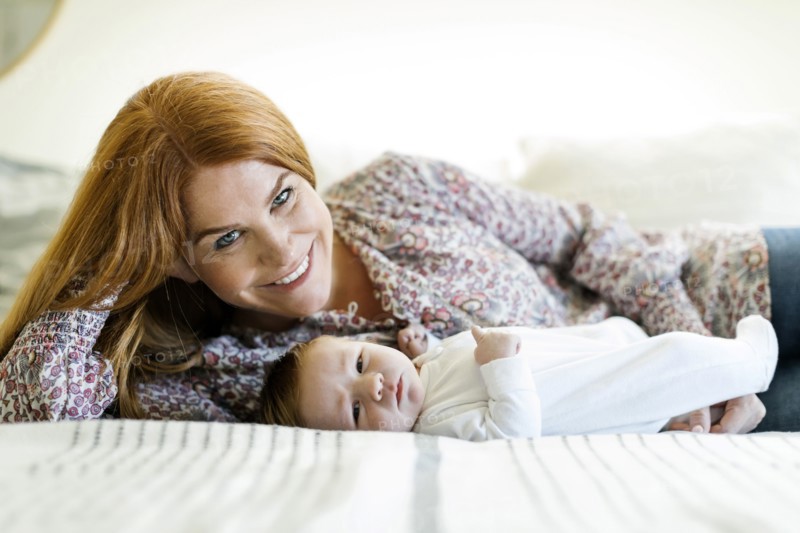 Smiling woman with her newborn son lying on a bed