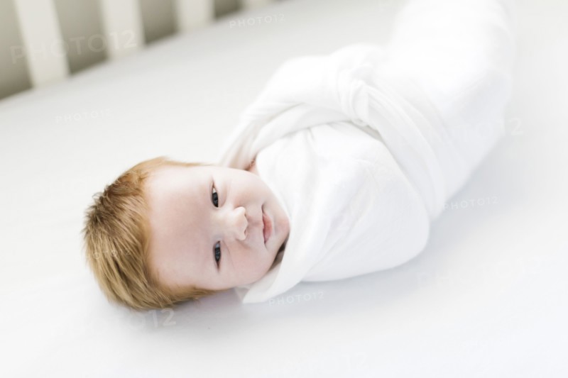 Swaddled baby boy in cot