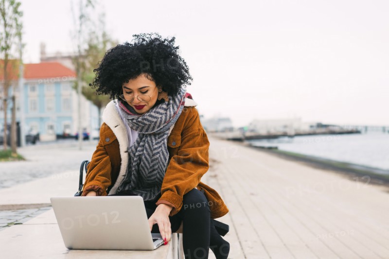 Young woman using laptop on waterfront in Lisbon, Portugal