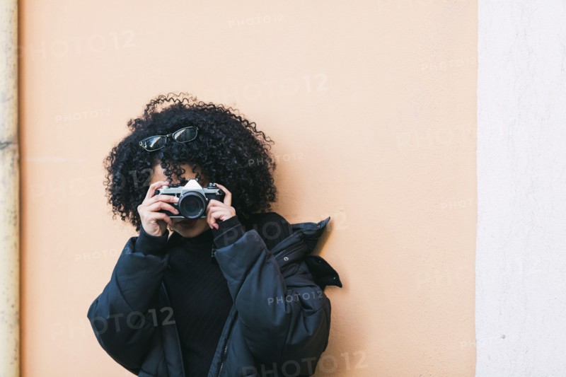 Young woman taking photograph against orange wall