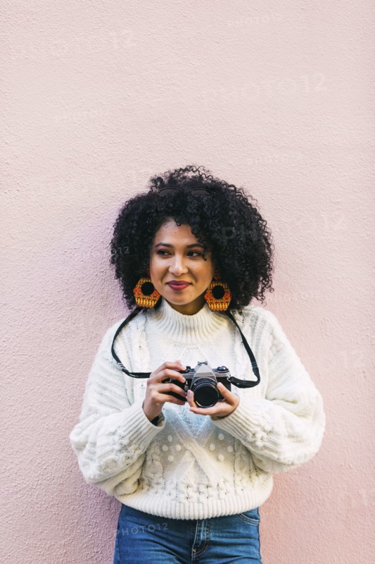 Young woman holding camera against pink wall