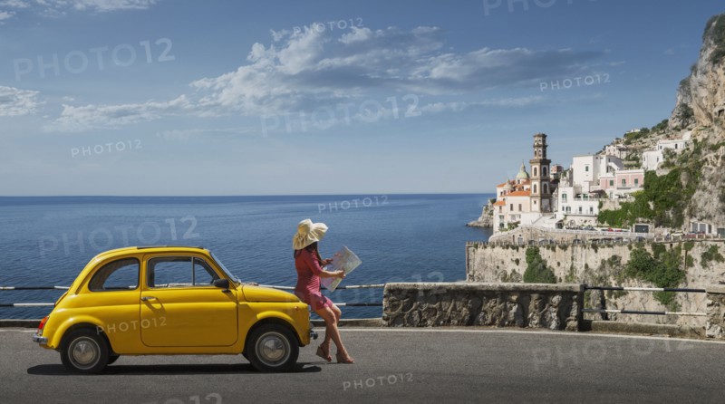 Woman holding map leaning on yellow car in Atrani, Italy
