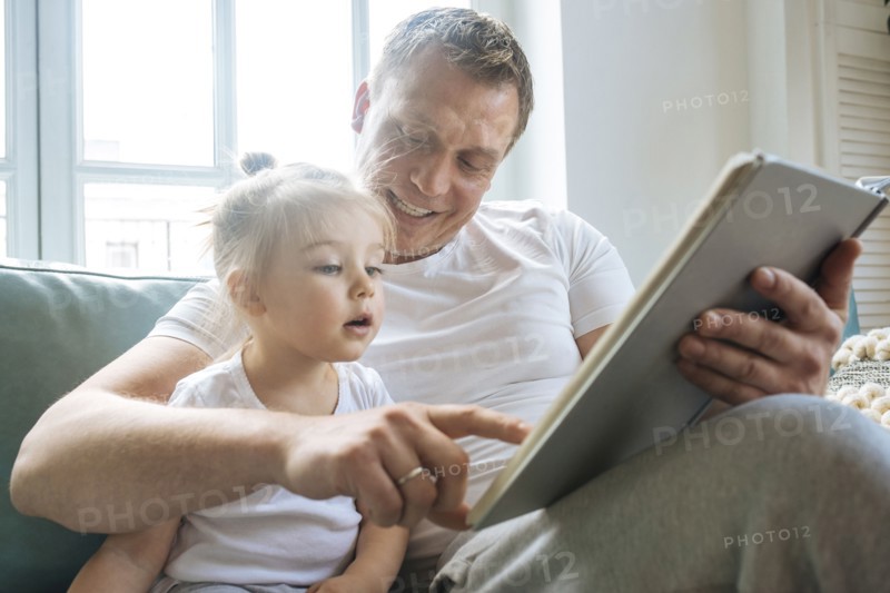 Father reading book to daughter on sofa