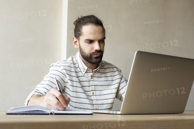 Young businessman with laptop writing in note pad