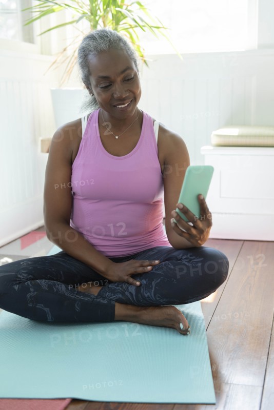 Mature woman with smart phone sitting on yoga mat