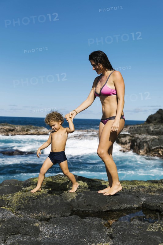 Mother and son walking on rocks by sea