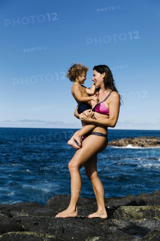Mother carrying her son on rocks by sea